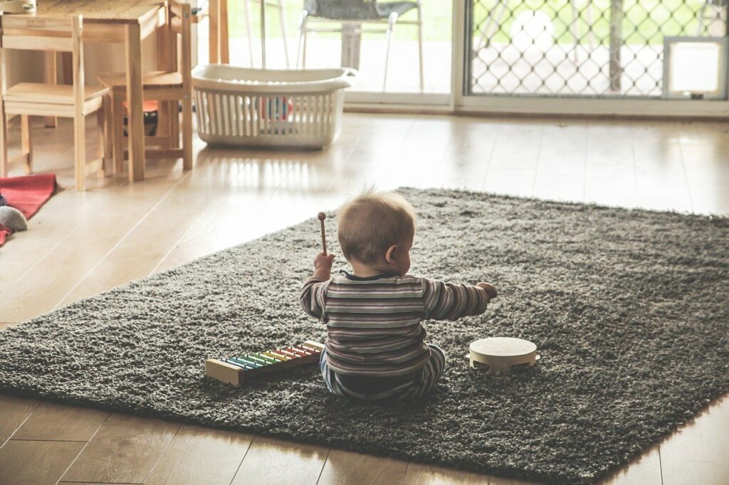 Welches Babyspielzeug ist sinnvoll Baby sitzt auf Teppich und spielt