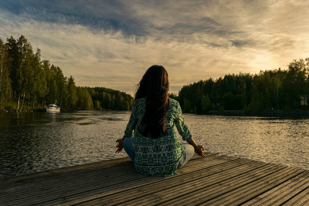 Frau meditiert draussen am Wasser Wie hilft Meditation bei der Kontrolle des Geistes