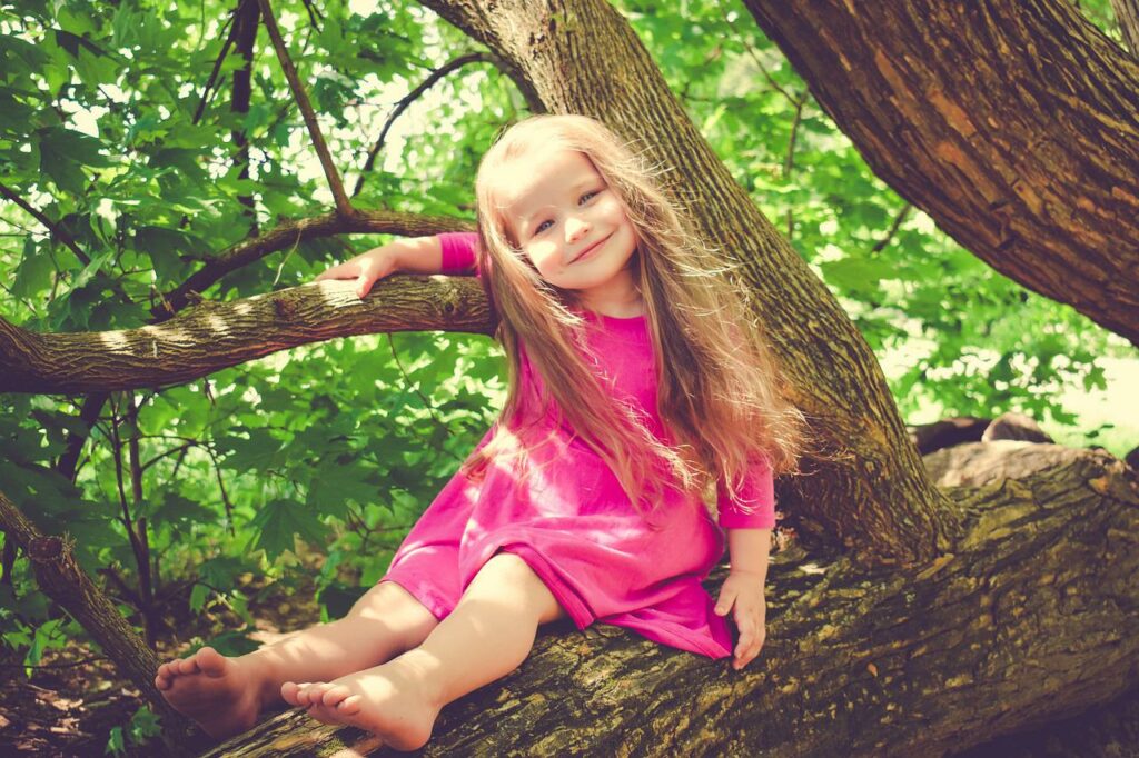 Kleines Mädchen klettert im Baum Strukturierte oder unstrukturierte Spiele für Kinder