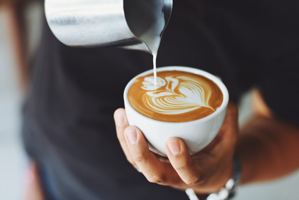 Barista gießt Milch in Kaffeetasse Kaffee Probierpaket - so entdecken Sie die Welt der Kaffeebohnen